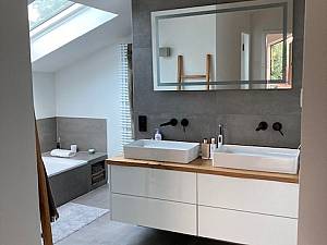 Aufsatzwaschbecken auf Holzkonsole, schwarze Armaturen, graues Feinsteinzeug Boden und Wände. 