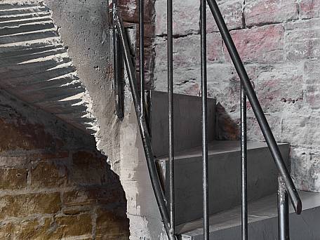 Gewendelte, rohe Stahlbetontreppe, in ein Gewölbe gebrochen, Stabstahlgeländer.